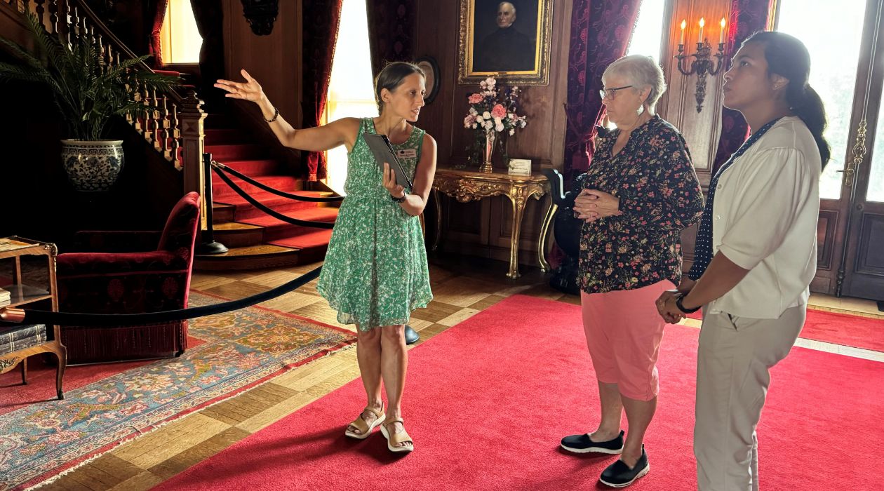 A female tour guide gestures with her hands as she speaks to two tour participants inside the Mills Mansion at Staatsburgh State Historic Site, Staatsburg